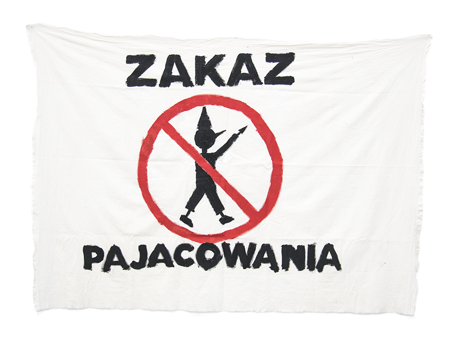 Zdjęcie. Biały transparent z napisem "ZAKAZ PAJACOWANIA" i rysunkiem przekreślonego pajacyka.