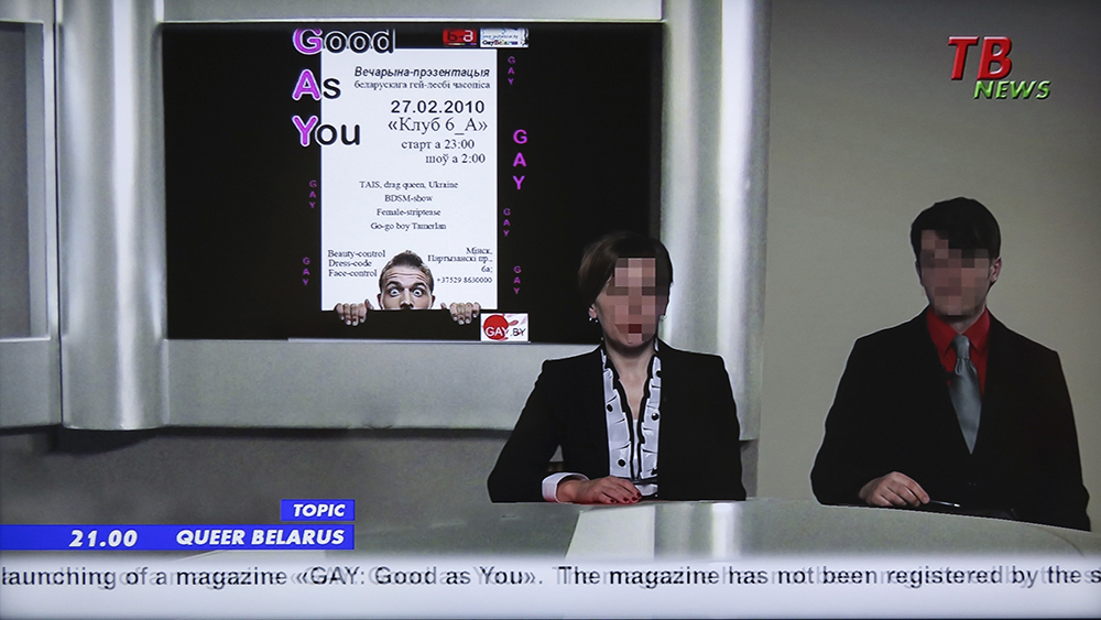 Kadr z filmu. Kobieta i mężczyzna prezentujący serwis informacyjny, oboje mają zapikselowane twarze.