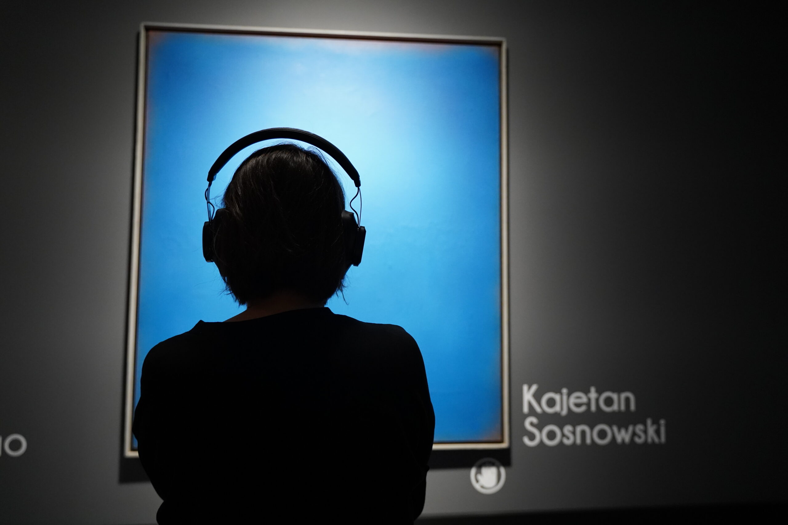 Wystawa „Kolekcja Dostępna”, kobieta słucha audiodeskrypcji do pracy Kajetana Sosnowskiego, „Błękitny obraz”, fot. Emilia Lipa.